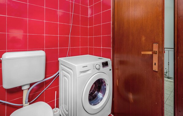 Ein kleines Badezimmer mit roter Fliesenwand, einer weißen Waschmaschine und einer Toilette.