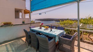 A terrace with a table set for dining, wicker chairs, a blue tablecloth, and a view of the sea.
