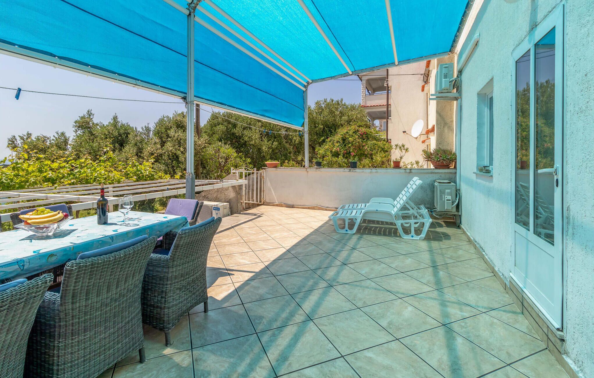 Une terrasse extérieure couverte, avec une table dressée pour les repas, des chaises en osier et un parasol bleu.