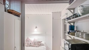 Ett smalt rum med en säng, en hylla med köksredskap och ett vitt tak.