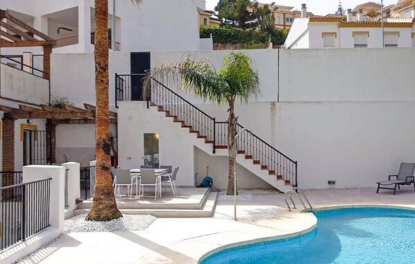 Zona de piscina con una palmera, mobiliario exterior y una escalera que lleva a un nivel superior.