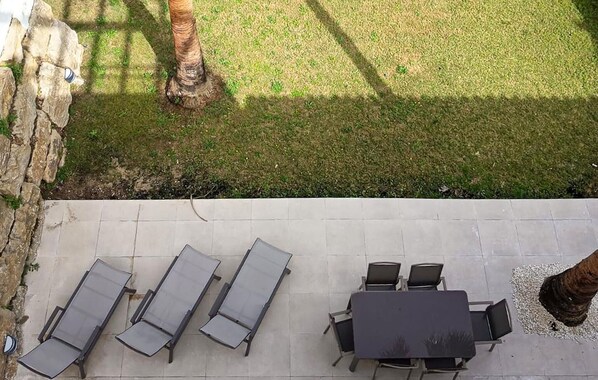 Un patio al aire libre con pared de piedra, césped y una mesa con sillas.