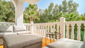 Ein Balkon mit einer Couch, einem kleinen Tisch mit Flasche und Gläsern sowie Blick auf Bäume und Grünflächen.