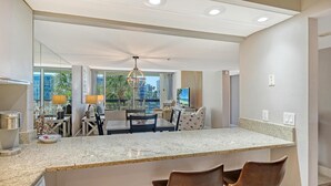 A modern hotel room with a kitchen area, dining space, and large windows offering a city view. - Stunning 2 BR Condo views of the Gulf and Lake (Longboat Key)