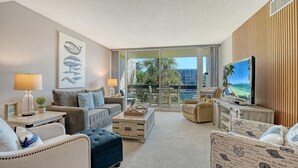 A modern living room with a balcony, a large TV, and a view of the city. - Stunning 2 BR Condo views of the Gulf and Lake (Longboat Key)