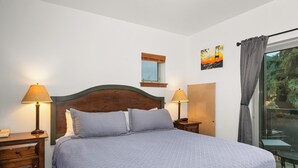 Un lit bien fait, avec une tête de lit en bois, deux tables de chevet avec des lampes, une fenêtre avec des stores et un tableau accroché au mur.