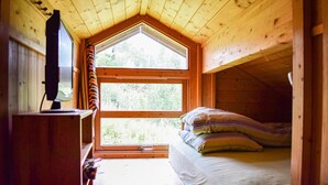 Ein gemütliches Cabin-Zimmer mit Bett, Fernseher und großem Fenster mit Blick ins Freie.