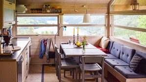 Ein gemütliches Blockhaus-Interieur mit Essbereich, Küche und Sitzgelegenheiten an großen Fenstern mit Blick auf eine malerische Landschaft.