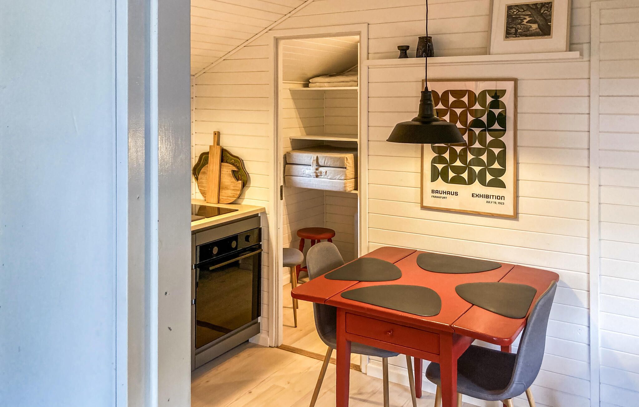 A compact kitchen with a built-in oven, a dining table with chairs, and a hanging pendant light.