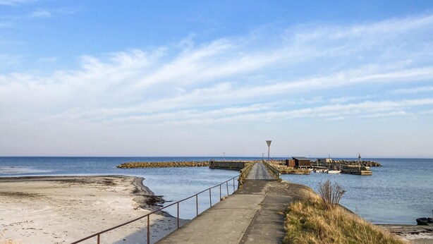 A coastal walkway leading to a pier with boats, a lighthouse, and a rocky breakwater. - 1 bedroom lovely home in Nexø (Nexø)