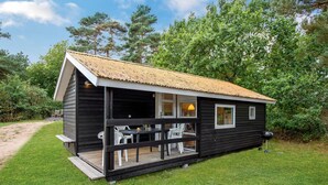A small, dark wooden cabin with a sloped roof, a porch with chairs, and a table. - 1 bedroom lovely home in Nexø (Nexø)