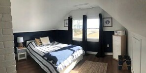 Cozy retreat with a large bed, bedside table, and dresser, set against a dark wall with a window and woven rug.