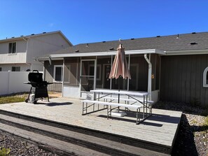 A house with a covered patio, a grill, and a table with chairs.