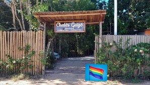 A wooden gate with a sign reading "Chalés Guigó" and a rainbow flag. - Chalés Guigó (Prado)
