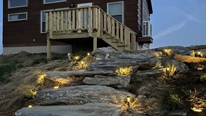 A modern house with a wooden deck and a stone staircase leading to a second-story entrance.