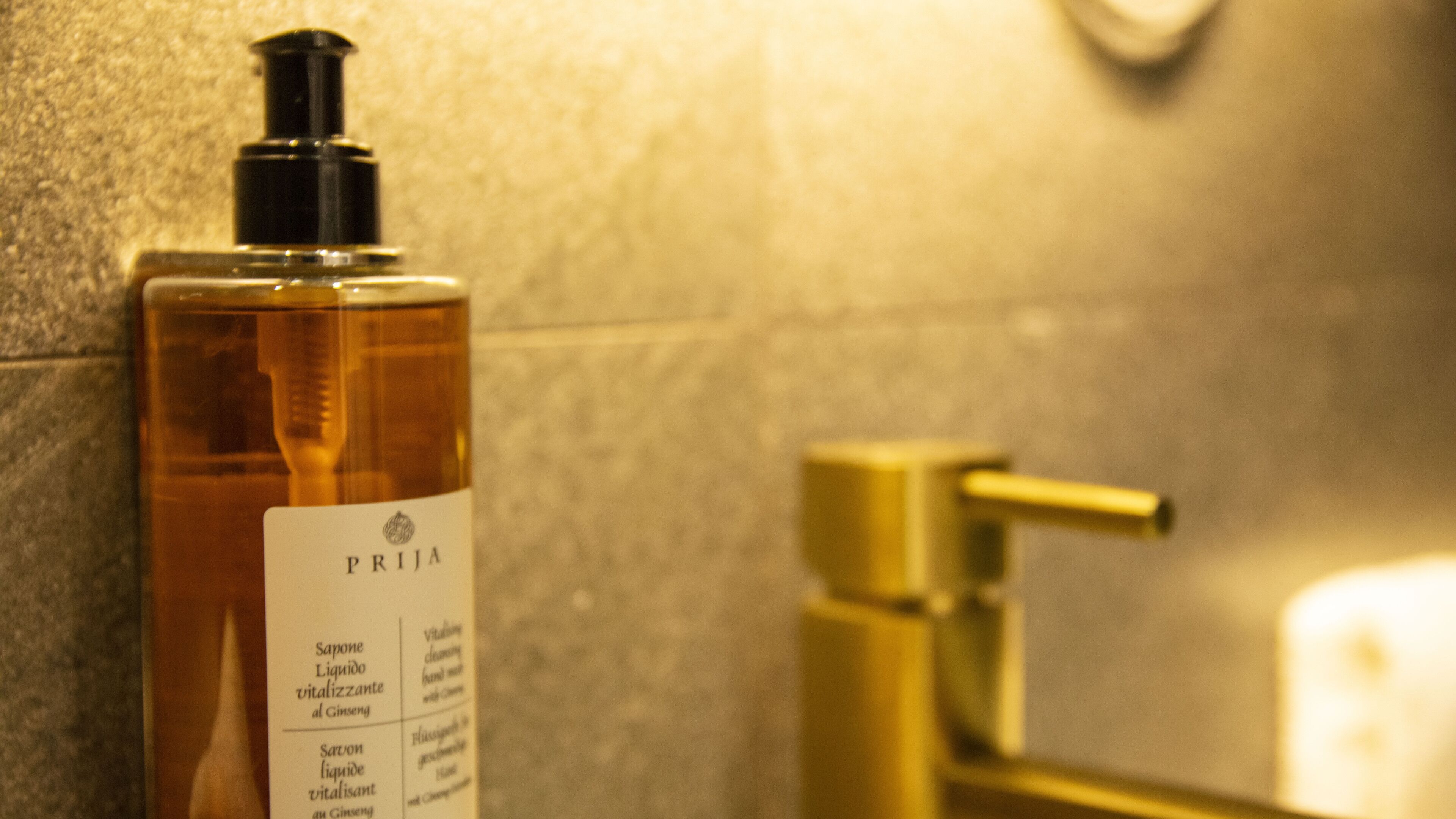 A bathroom with a bottle of PRIJA soap and a gold faucet.