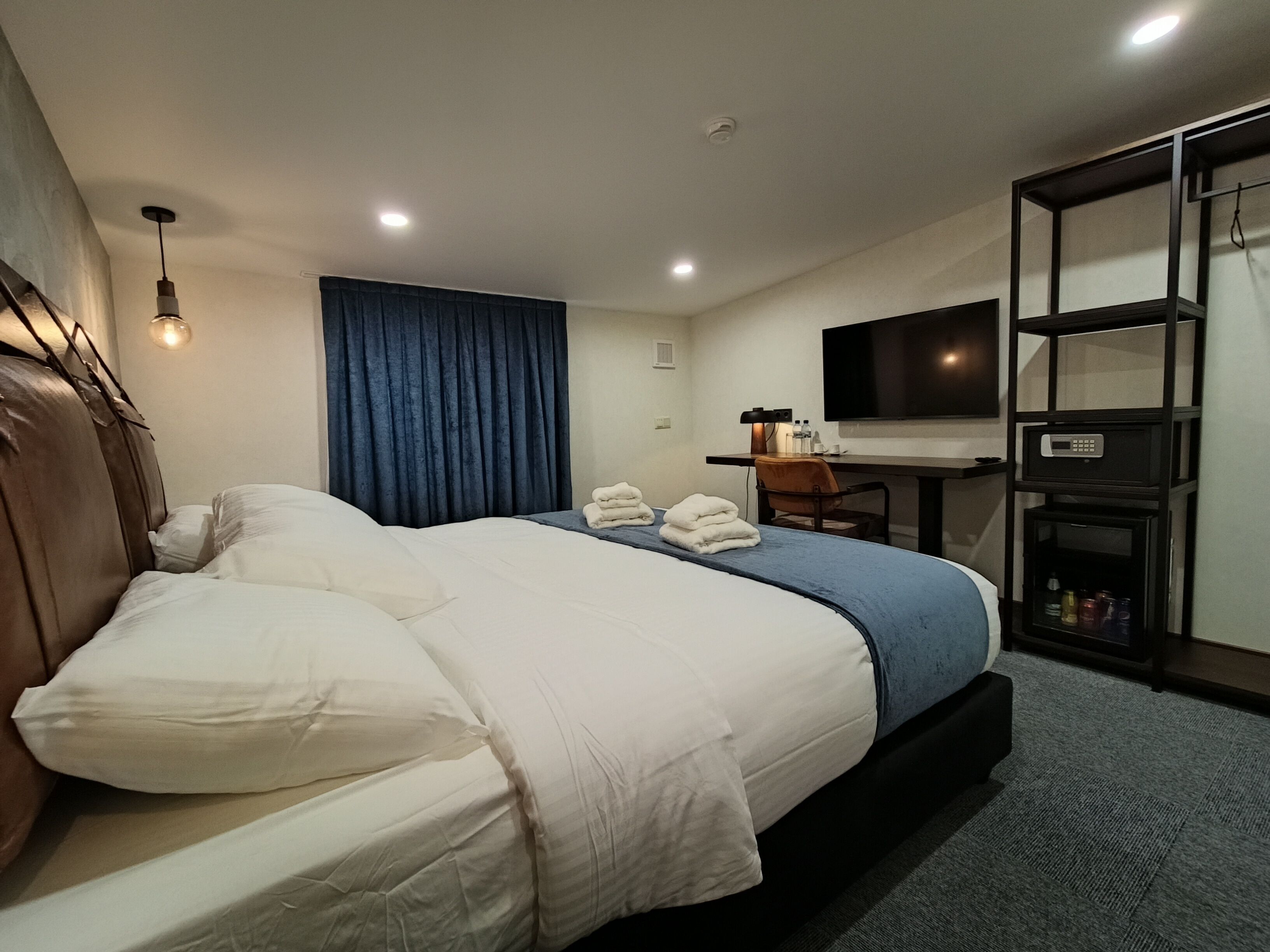 Habitación de hotel con una cama, un escritorio, un televisor y una estantería con botellas.