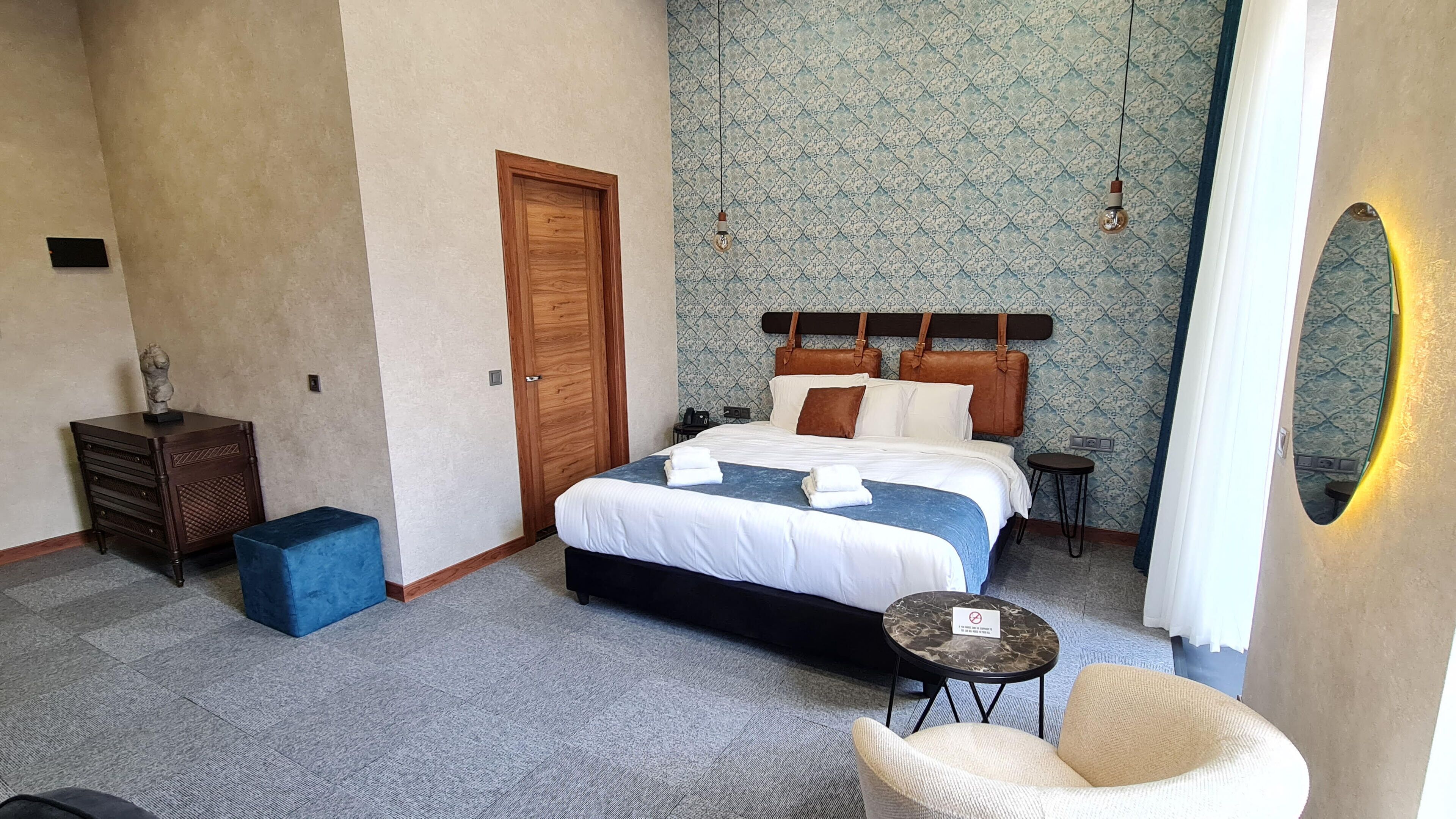 A hotel room with a bed, a small table, a chair, a nightstand, and a door.