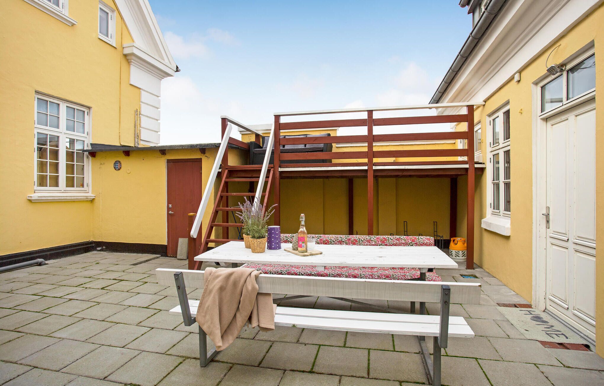 A patio with a table and bench, a ladder, and a door leading to a yellow building.