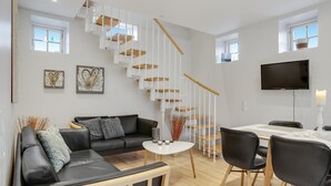 A modern living room with a black leather sofa, a white coffee table, and a wooden staircase. - 3 bedroom beautiful home in Skagen (Skagen)