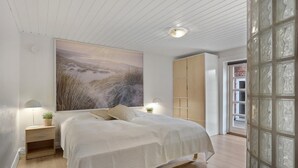 Une chambre à coucher avec un grand lit, deux tables de chevet avec des lampes, un tableau accroché au mur et une armoire en bois.