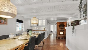 Un espace repas avec une longue table en bois dressée pour le repas, un luminaire suspendu et une cheminée en briques en arrière-plan.