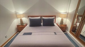 Une chambre à coucher avec un grand lit, deux tables de chevet avec des lampes, un miroir et un luminaire au plafond.