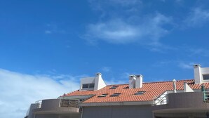 Un bâtiment doté d’un toit recouvert de tuiles rouges, de nombreuses cheminées et surplombant un ciel bleu clair parsemé de quelques nuages.