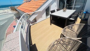 Un balcon avec une table et des chaises, une vue sur la plage et un toit recouvert de tuiles.