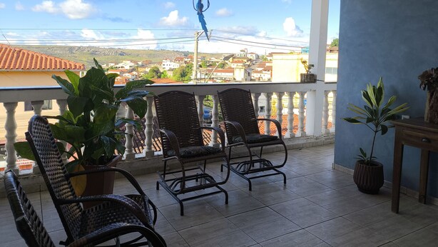 A balcony with wicker chairs and potted plants, overlooking a cityscape. - HOTEL VILLA REAL (Diamantina)