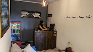 Un área de recepción con un sofá, un refrigerador de Coca-Cola, una laptop sobre un escritorio de madera y una pared con un cartel.