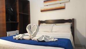 A hotel room with a bed, a blue blanket, a wooden headboard, a wall-mounted painting, and a wardrobe. - HOTEL VILLA REAL (Diamantina)
