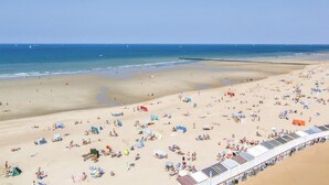 Ein Strand mit vielen Liegen und Sonnenschirmen, einem klaren Himmel und ruhiger See.