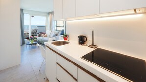 Eine moderne Küche mit eingebautem Herd, einer Kaffeemaschine und Blick auf einen Balkon mit Stuhl und Blumen.
