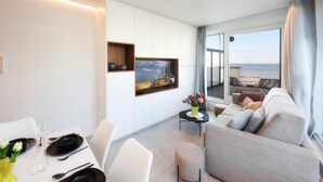 Ein modernes Wohnzimmer mit einer Couch, einem Esstisch und Blick auf den Strand durch ein großes Fenster.