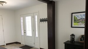 Un couloir avec une porte blanche, un banc noir et un tableau encadré accroché au mur.