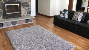 Un salon avec une cheminée en pierre, un canapé en cuir noir et un tapis à motifs gris.