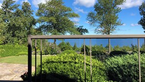 Un balcon doté d’une rambarde en métal, donnant sur un jardin et une étendue d’eau.