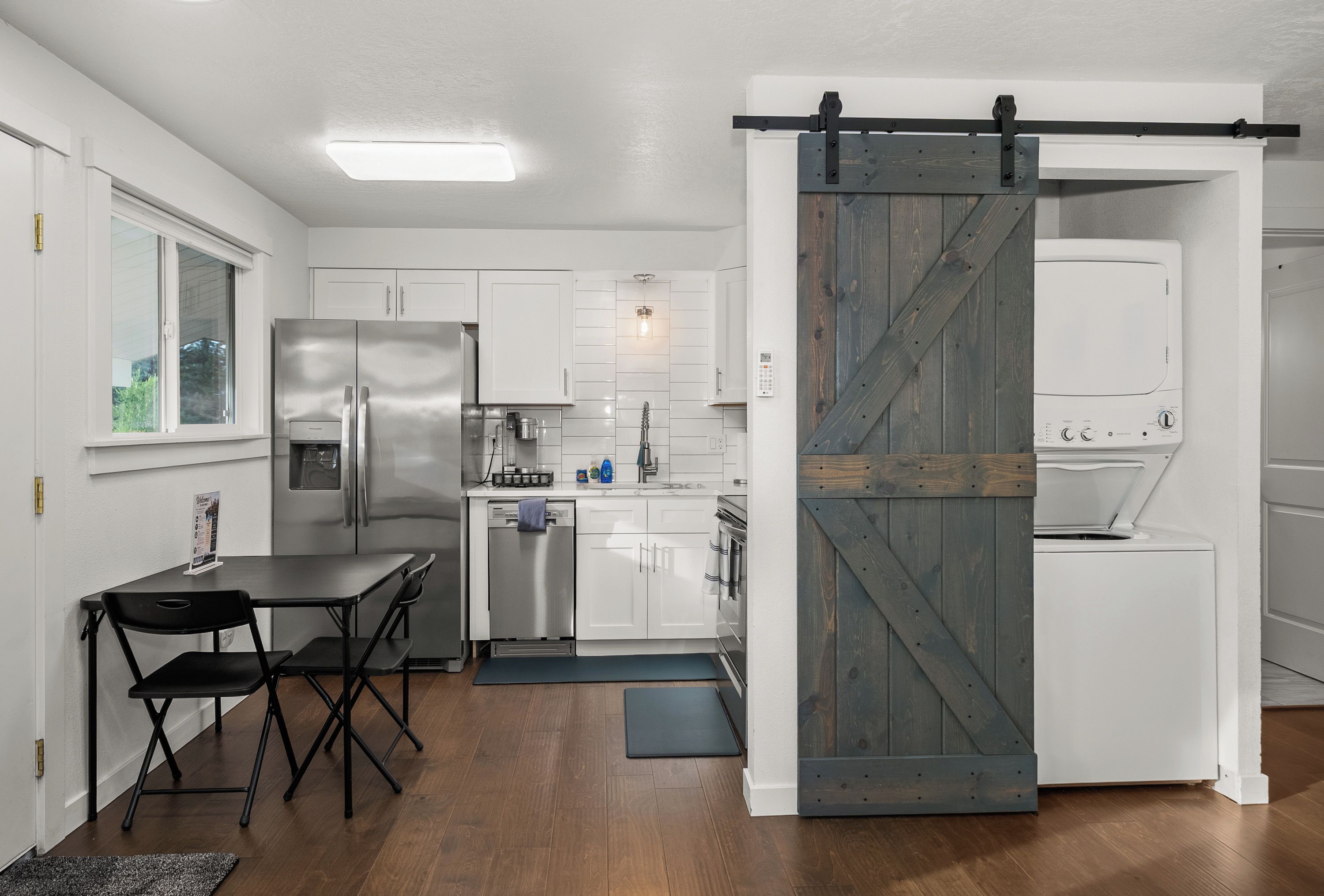 A modern kitchen with a sliding barn door, stainless steel appliances, and a dining area with a foldable table and chairs.