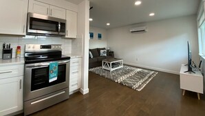 A modern kitchen with white cabinets, a stainless steel oven, and a microwave. There is a dining area with a white table and chairs, and a living room with a sofa and a coffee table. - 🏖 🏐 Upstairs Valley Beach Escape Apartment 🛹 💦 🏀 (Spokane Valley)