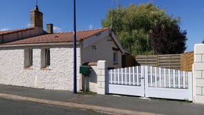 A white stone building with a tiled roof, a white picket fence, and a green mailbox.