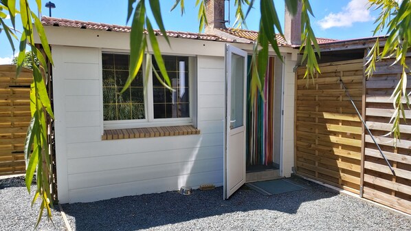 A small, white, single-story building with a window and a door, surrounded by gravel and wooden fencing.