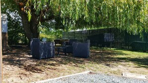 An outdoor seating area with wicker furniture under a large tree, a black fence, and a gravel path.