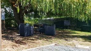 An outdoor seating area with wicker furniture under a large tree, a black fence, and a gravel path.
