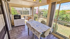Eine sonnendurchflutete Terrasse mit Tisch und Stühlen, einer Mikrowelle und Blick auf einen Garten.