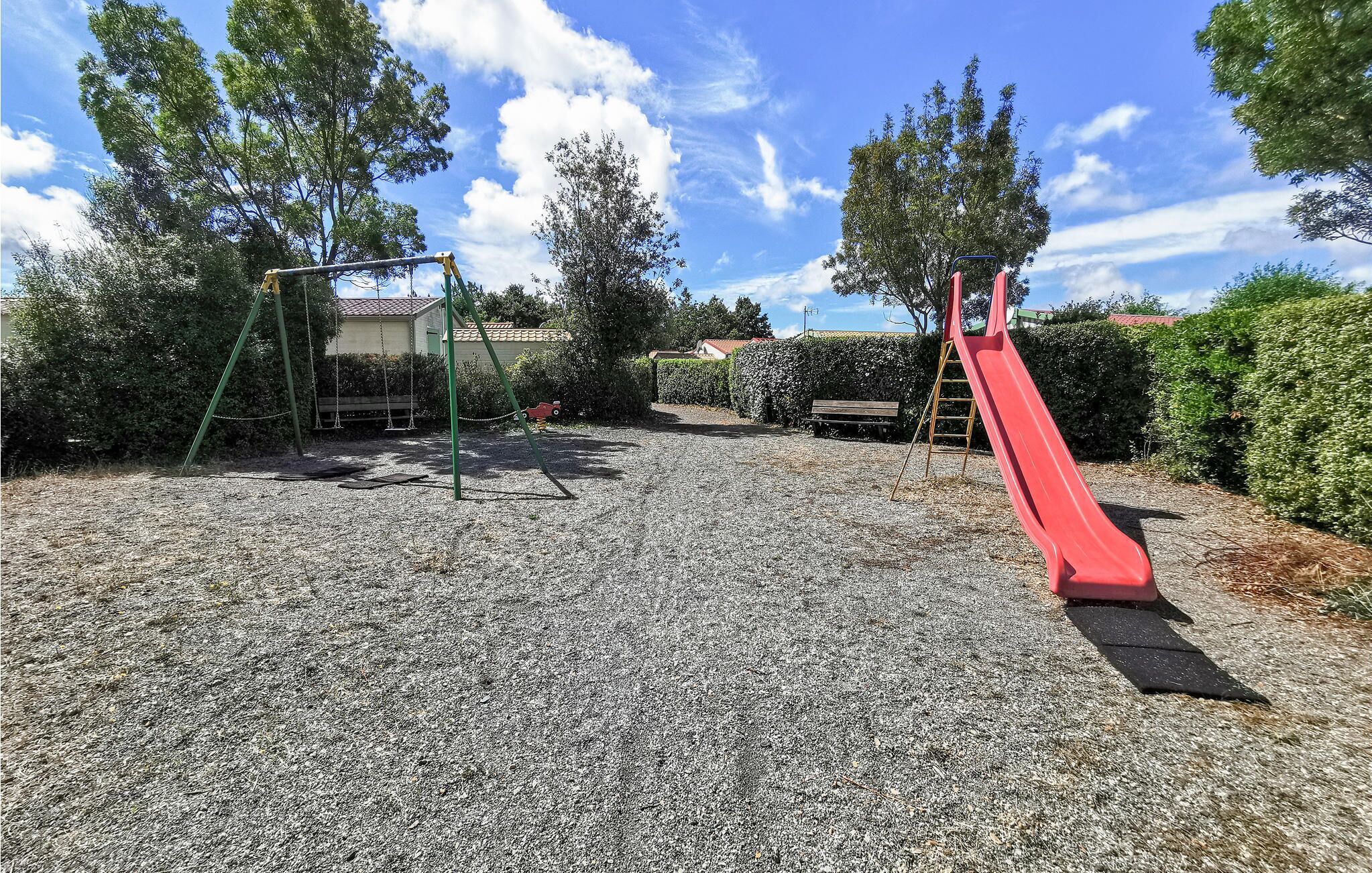 A playground with a red slide and swings, surrounded by trees and a clear sky.