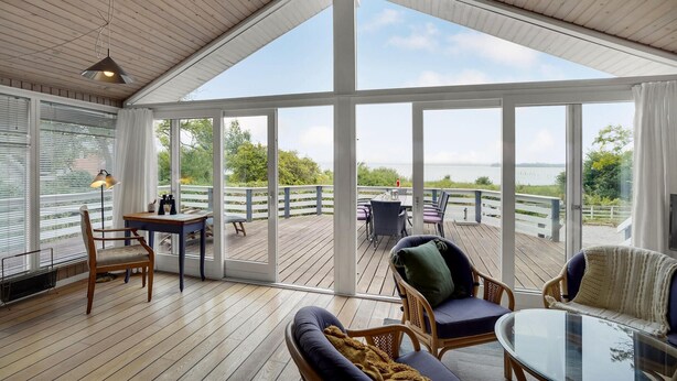 A spacious deck with a wooden floor, a glass-enclosed room with a table and chairs, and a view of the sea. - Amazing home in Broager with kitchen (Broager)