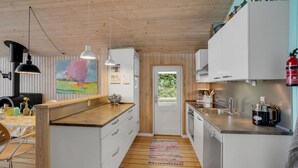 A modern kitchen with white cabinets, a wooden countertop, and a stove. There is a dining area with a table and chairs, and a colorful painting on the wall. - Amazing home in Broager with kitchen (Broager)