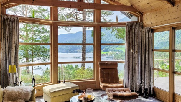 A cozy room with large windows offering a scenic view of a lake and mountains. - 4 bedroom stunning home in Hebnes (Hebnes)