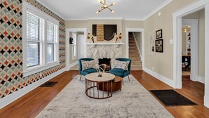 Un salon avec une cheminée, deux fauteuils bleus, une table basse ronde et un mur décoré de motifs.